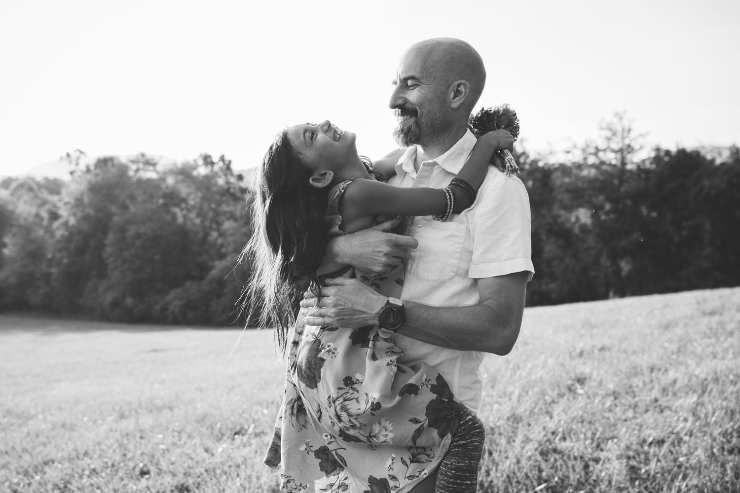 A black and white photo of a father and daughter sharing a playful moment in an open field.