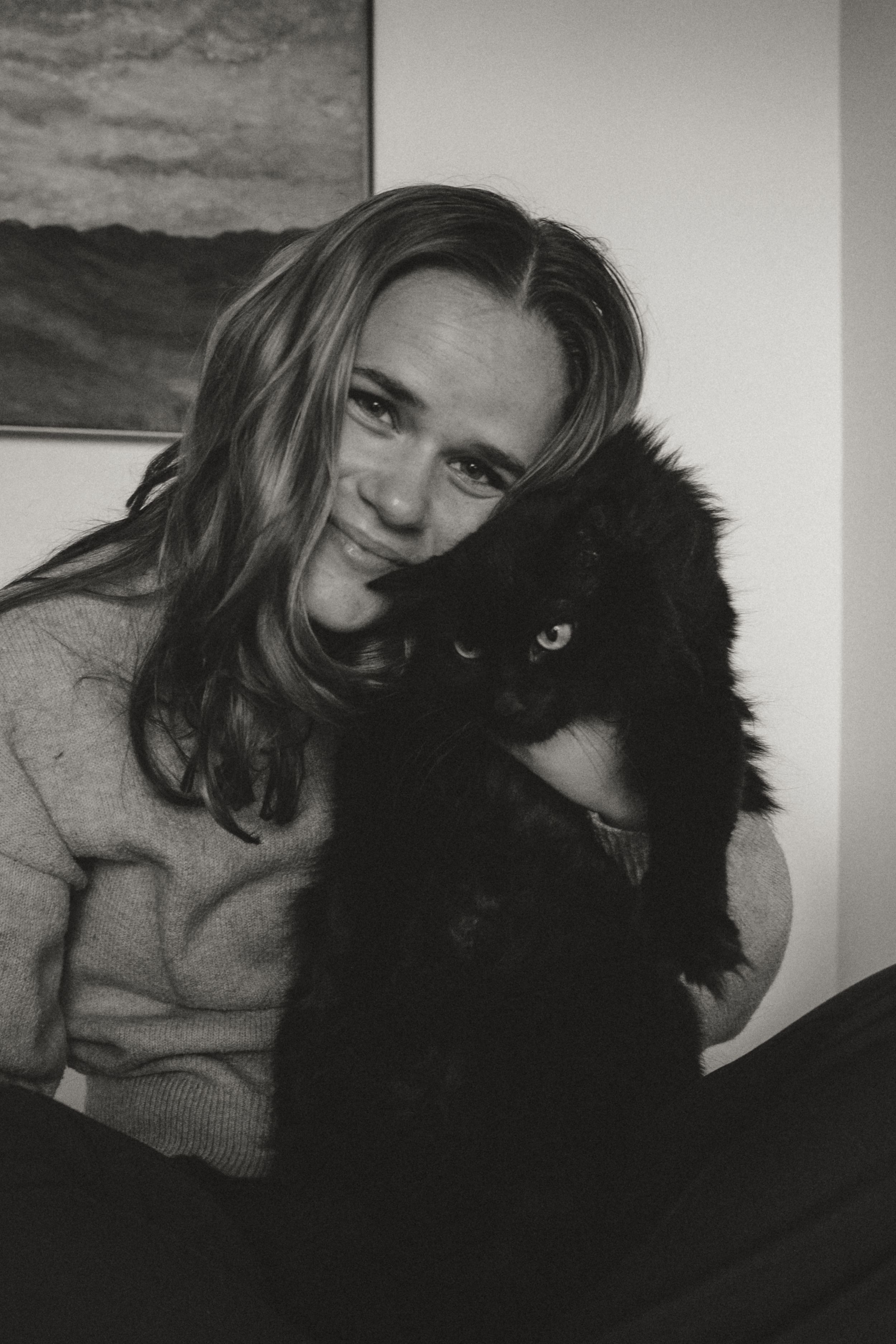 A black-and-white photograph shows someone in a sweater holding a fluffy black cat with bright eyes.