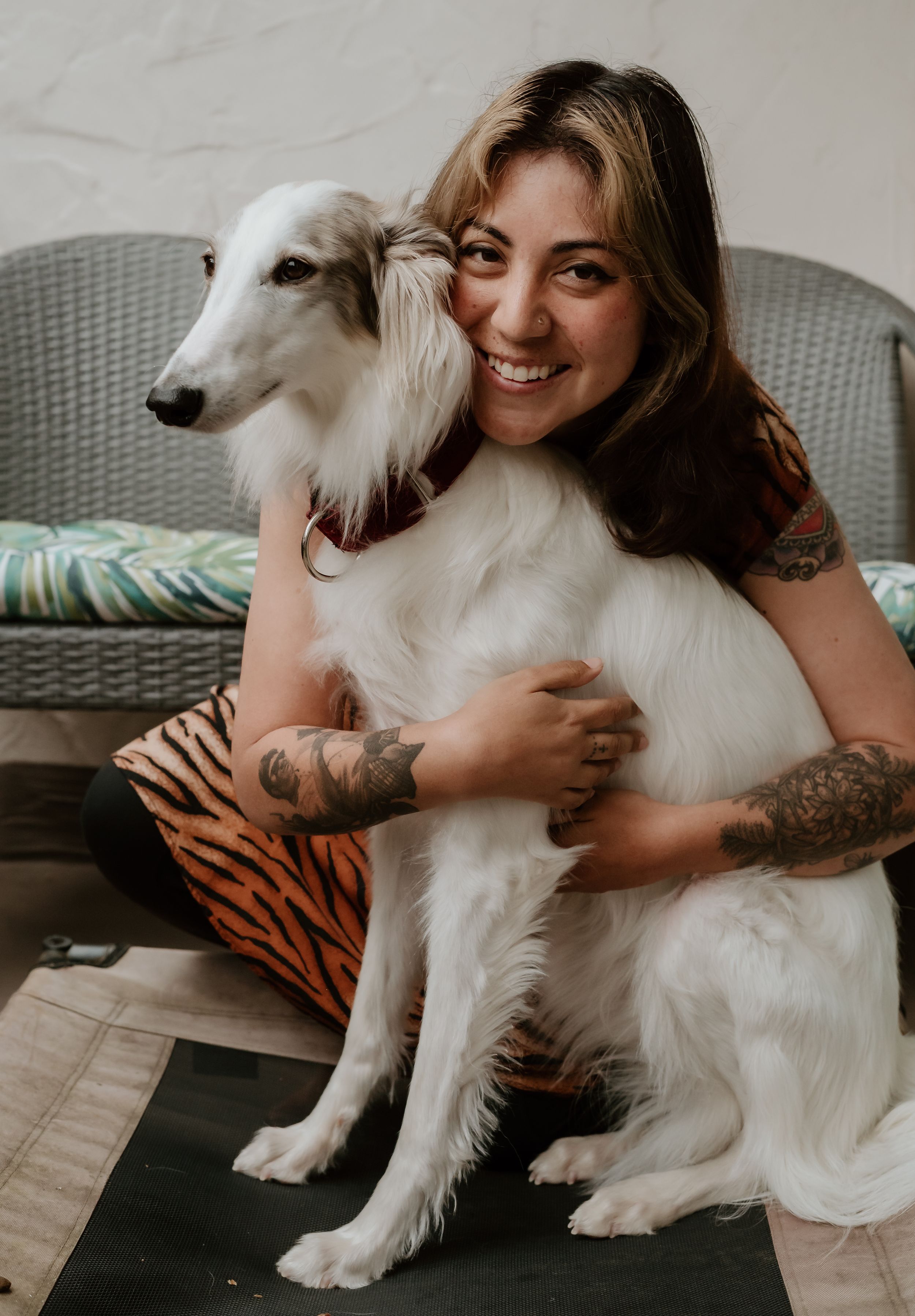 A person and white Borzoi dog cuddle together on a wicker chair with a casual, relaxed vibe.