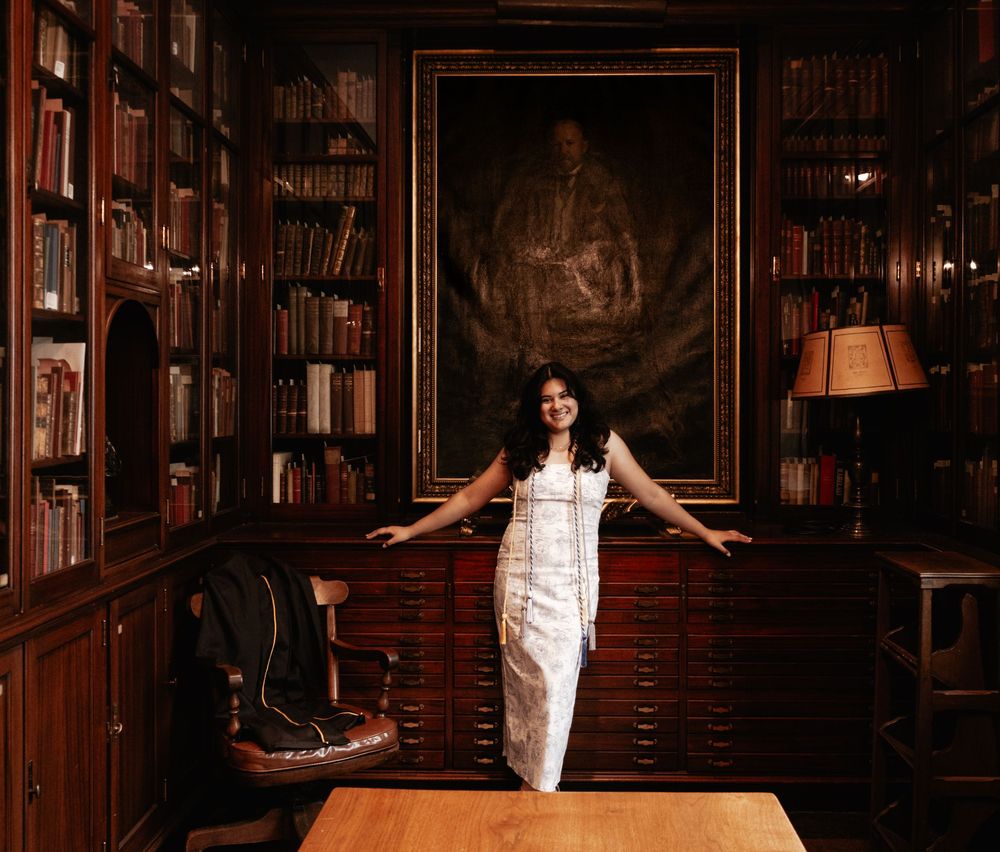 Woman in white dress poses dramatically in a dark wooden library with vintage decor and shelves of books.