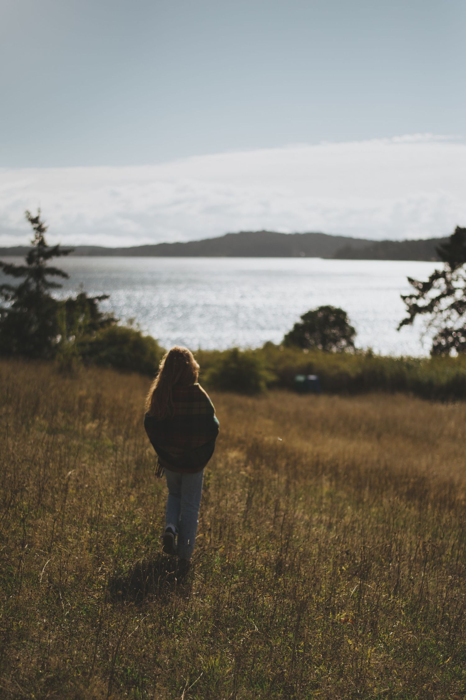 Silhouette standing in a coastal meadow at sunset overlooking the water.