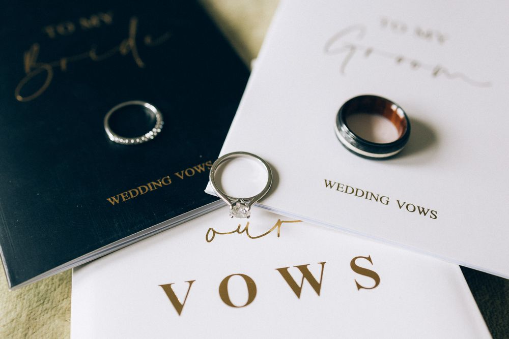 Wedding vows book and rings arranged on elegant paper with gold lettering.