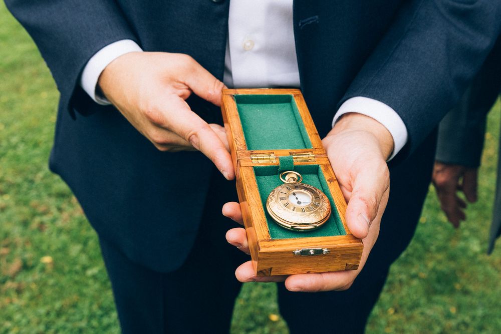 Hands hold wooden box containing vintage pocket watch against grassy background.