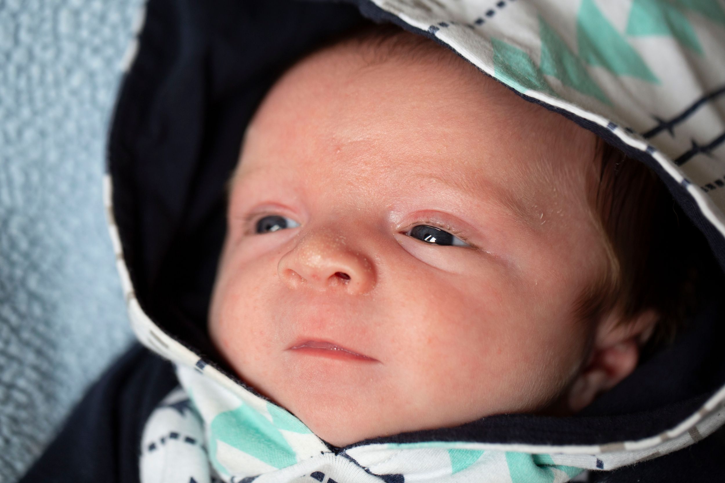 Newborn baby bundled in a hooded blanket with geometric print, gazing softly at the camera.