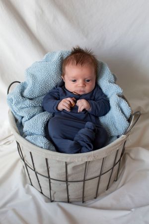 Newborn baby in navy outfit resting in a wire basket lined with a soft blue blanket.