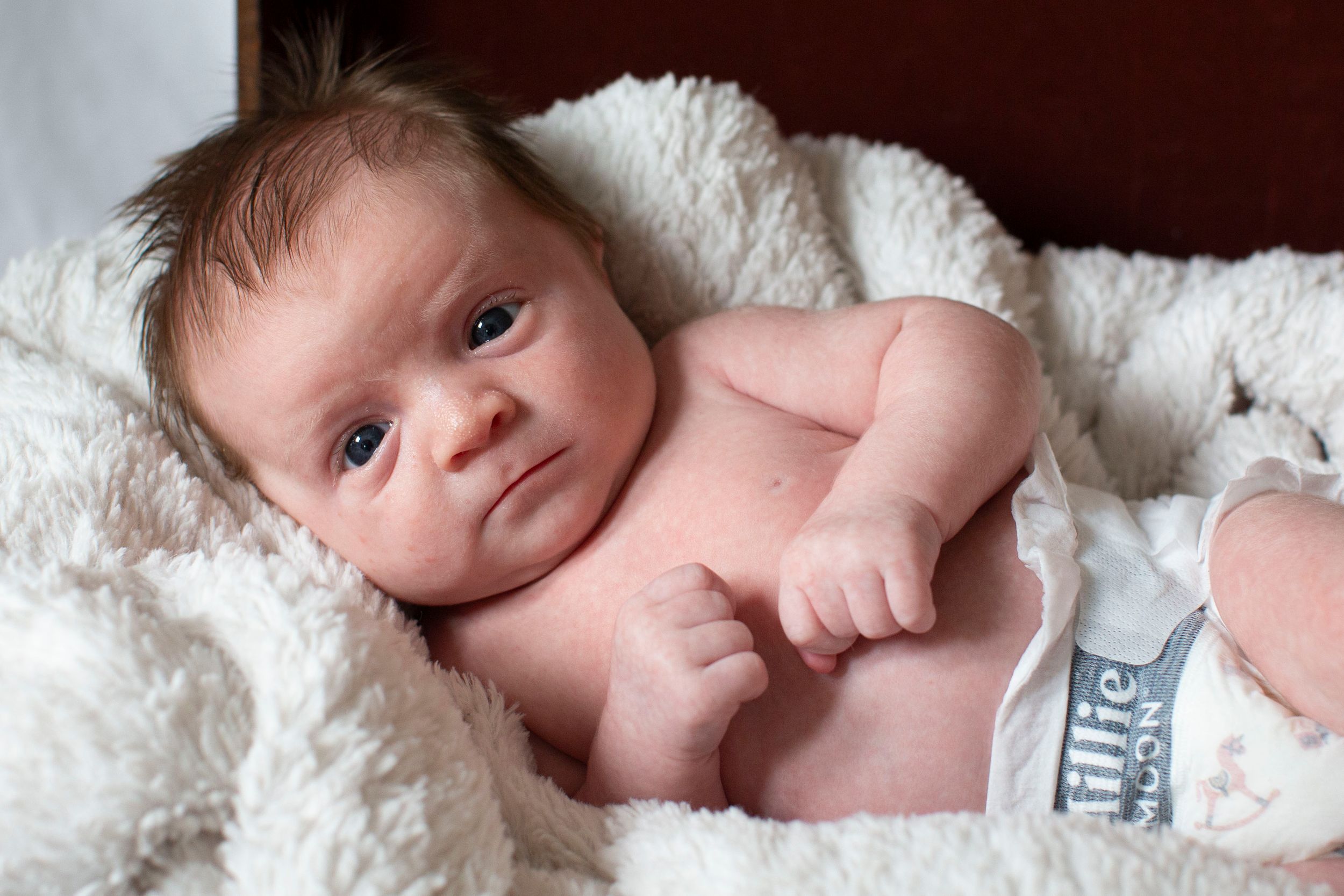 Peaceful newborn baby lying on a soft white blanket wearing a diaper.
