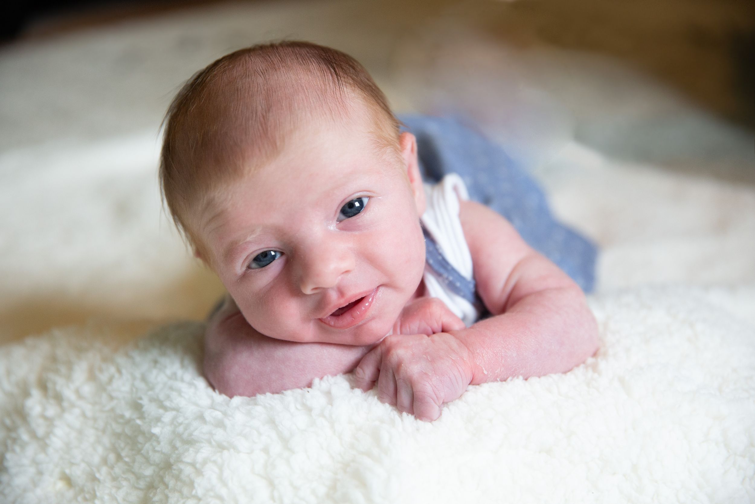 Newborn baby lying on a fluffy white blanket, looking up with bright eyes and a gentle smile.