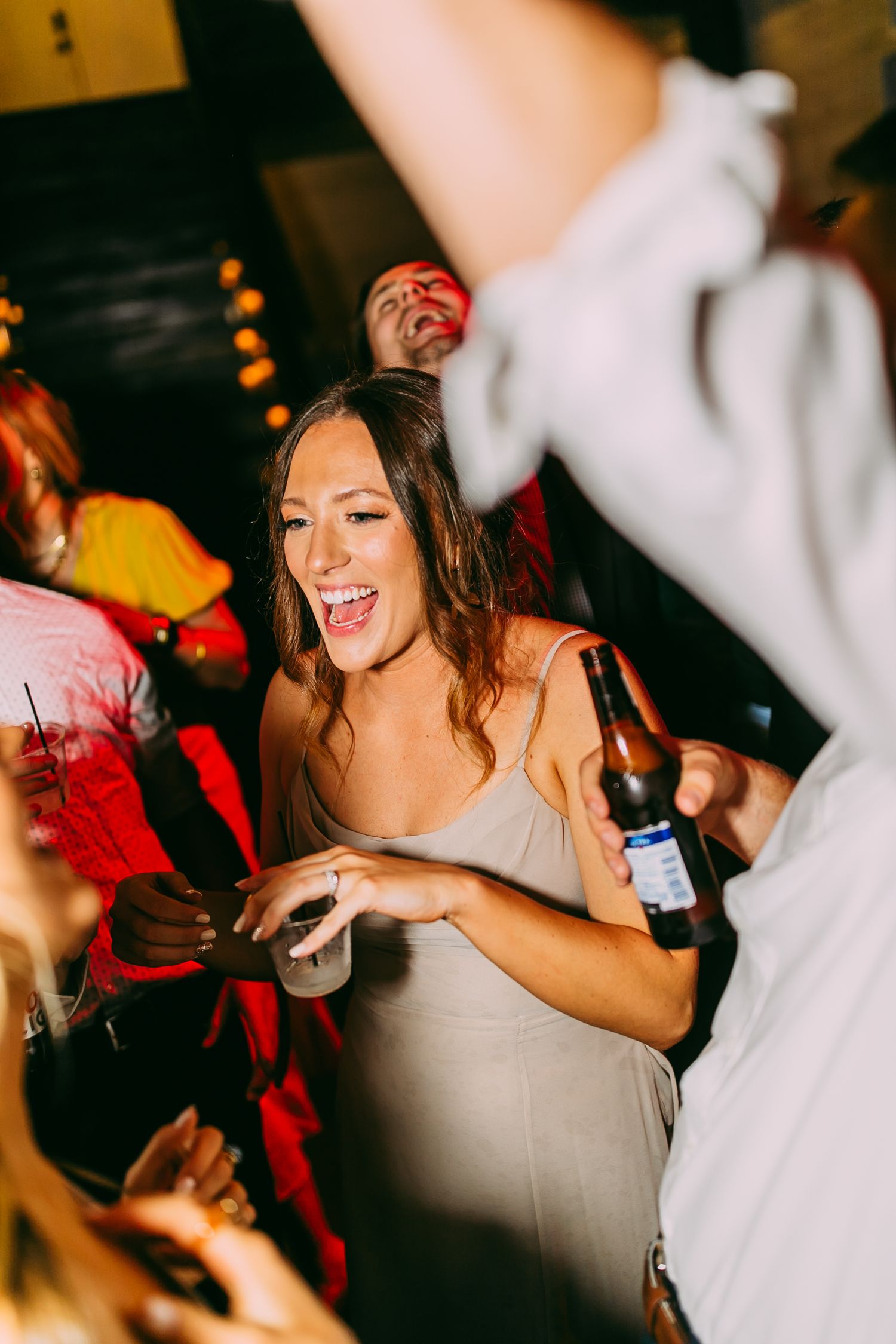 Party guests dancing and celebrating with drinks in a dimly lit venue.