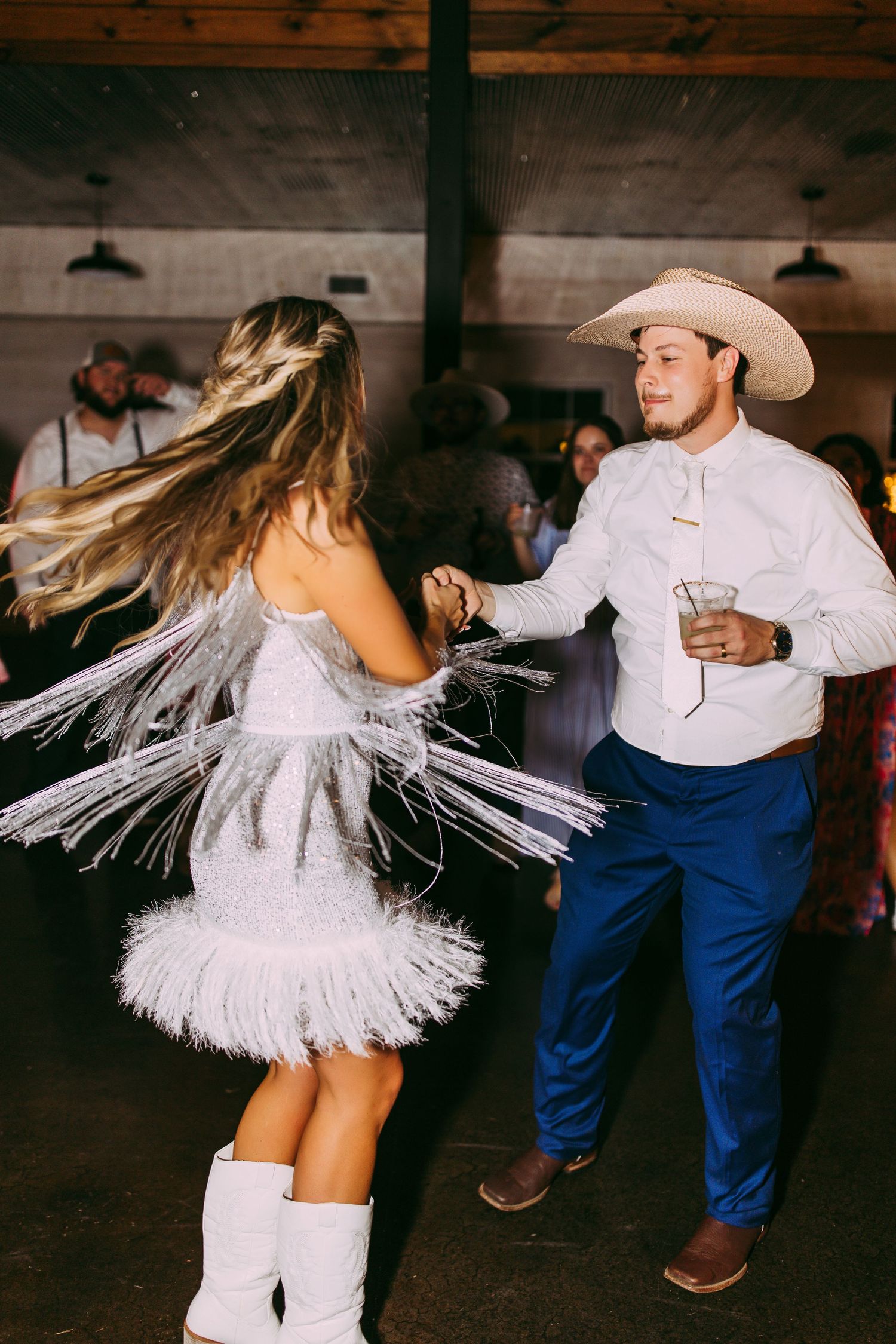 Couple dancing at a western-themed event with the woman in a white fringe dress and man in cowboy attire.