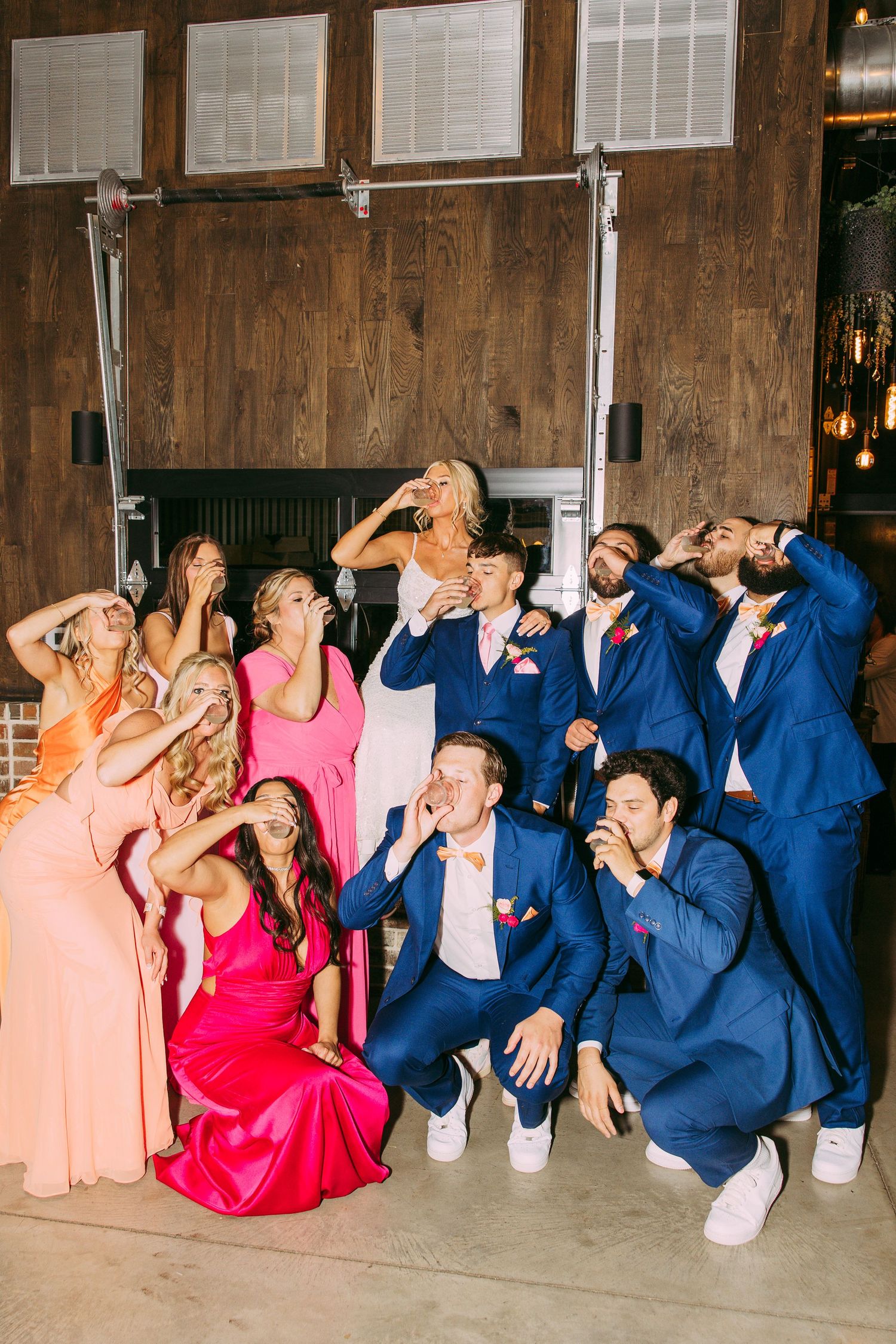 Wedding party strikes fun pose taking shots together in rustic wooden venue.
