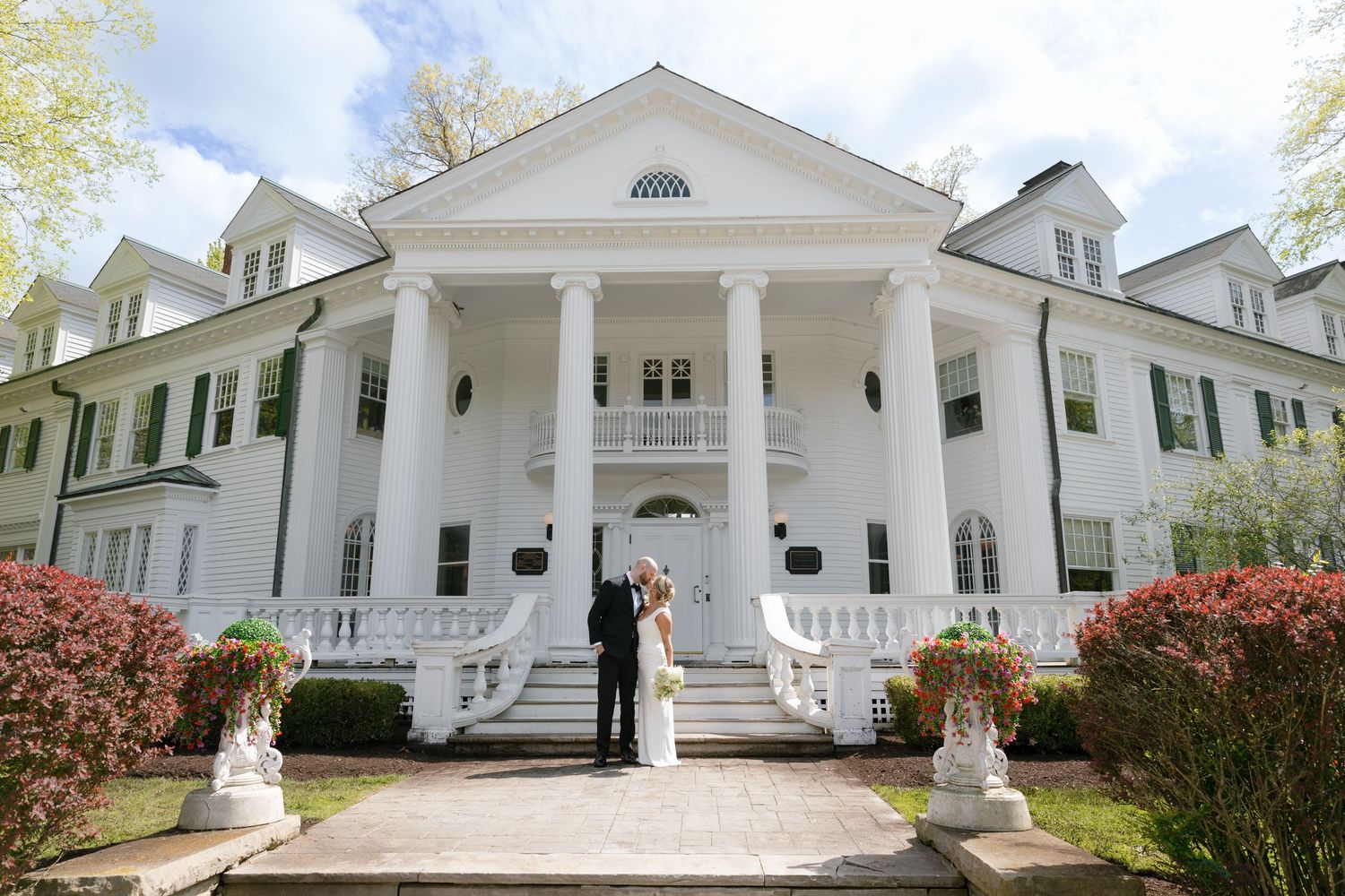Wedding guests mingle at an outdoor reception through glass windows at dusk.