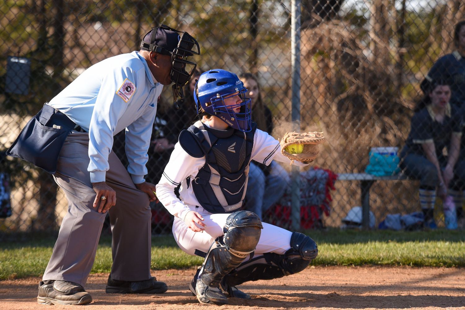 Baseball game action shot with catcher and umpire at home plate during sunny day.