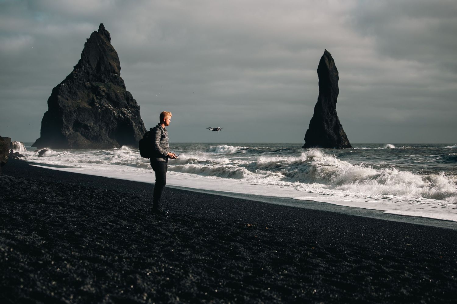 Silhouette of figure standing on black sand beach with dramatic rock formations in Iceland.