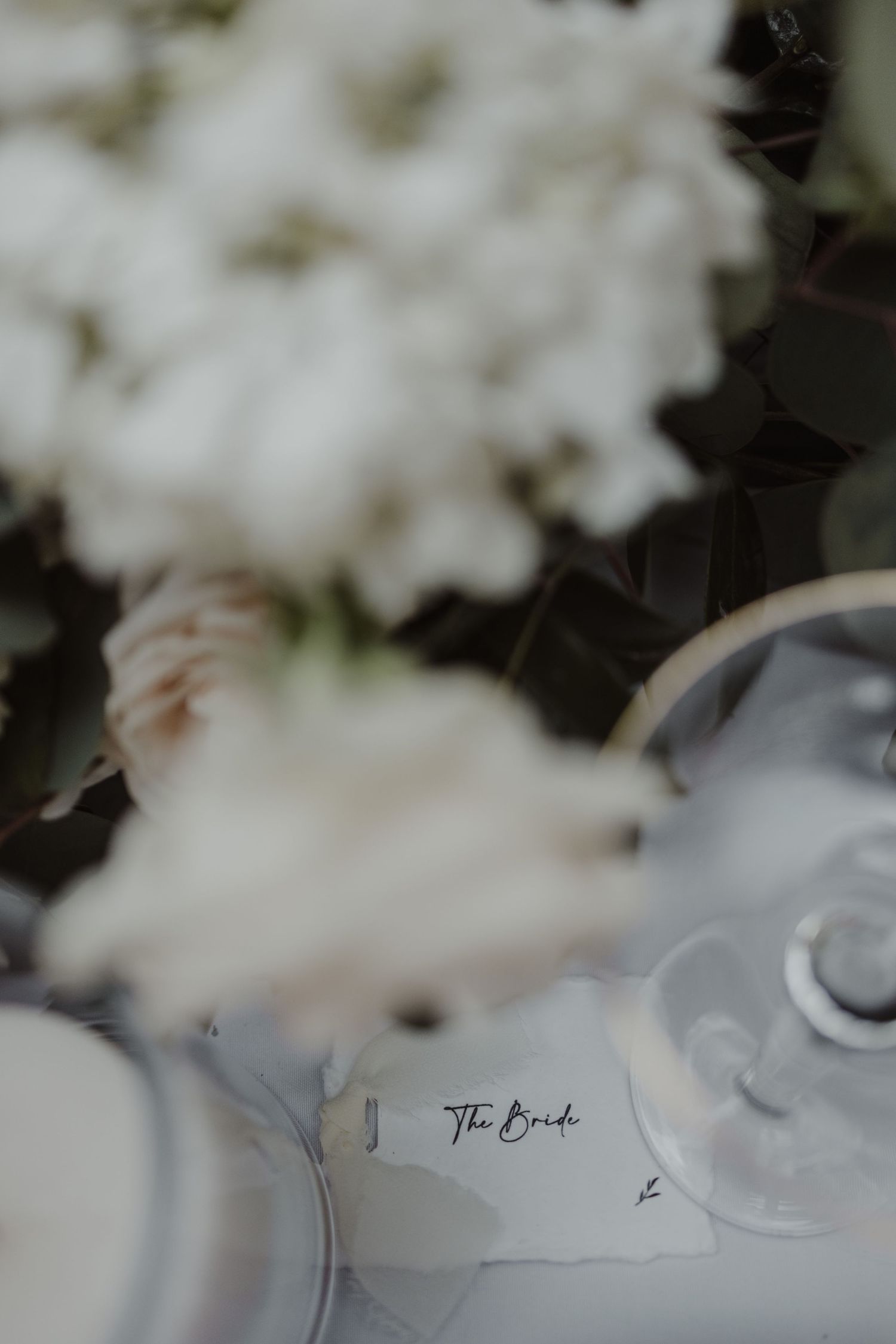Elegant wedding table setting with a bride place card surrounded by soft white floral arrangements.