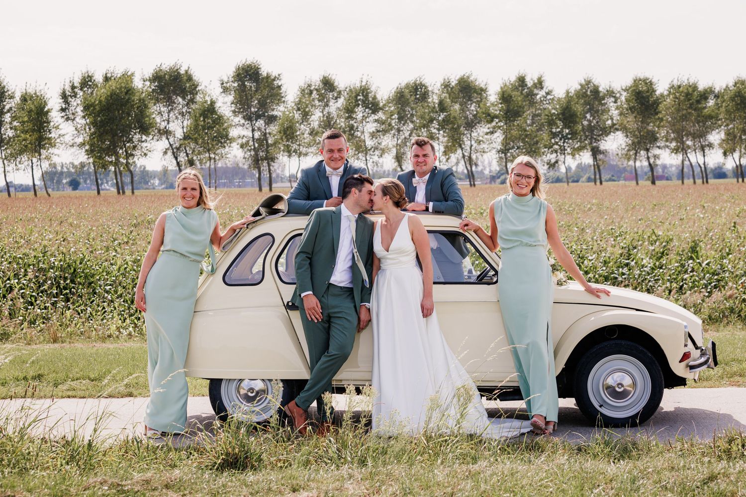 Wedding party posing with a classic vintage car on a country road.