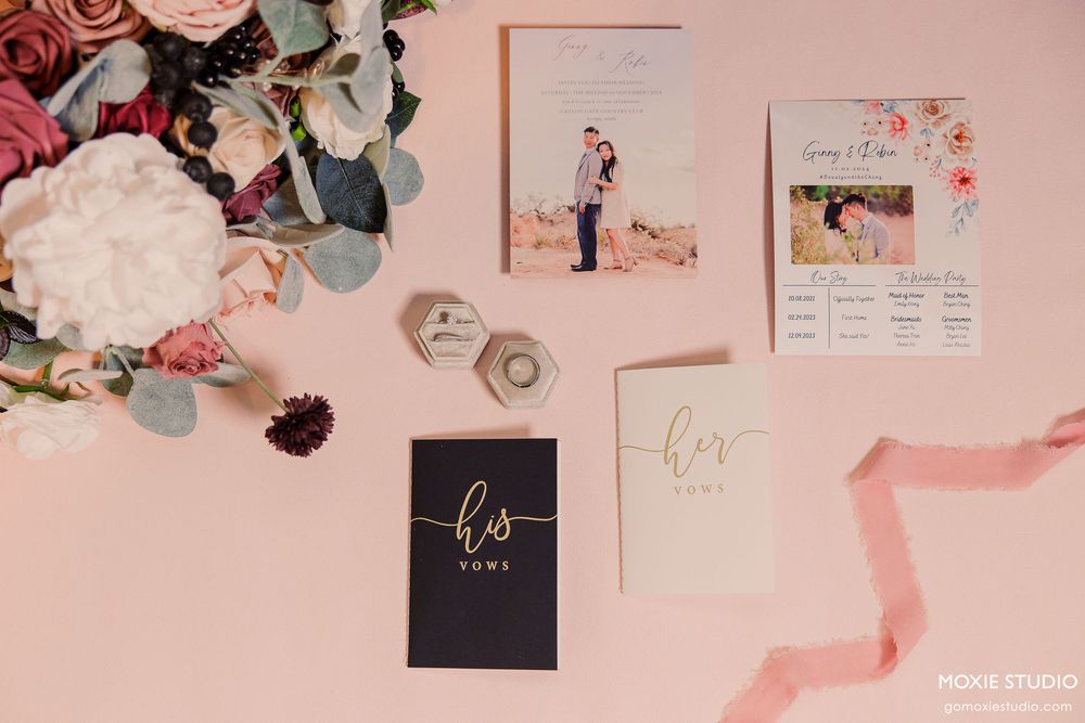 A romantic pink and gold wedding stationery flatlay with roses, eucalyptus leaves, and delicate ribbons.