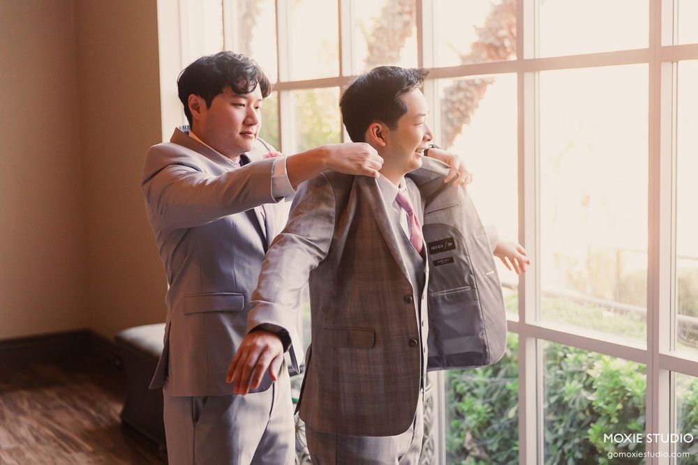 A group of students wearing school uniforms stand by large windows in a bright hallway.
