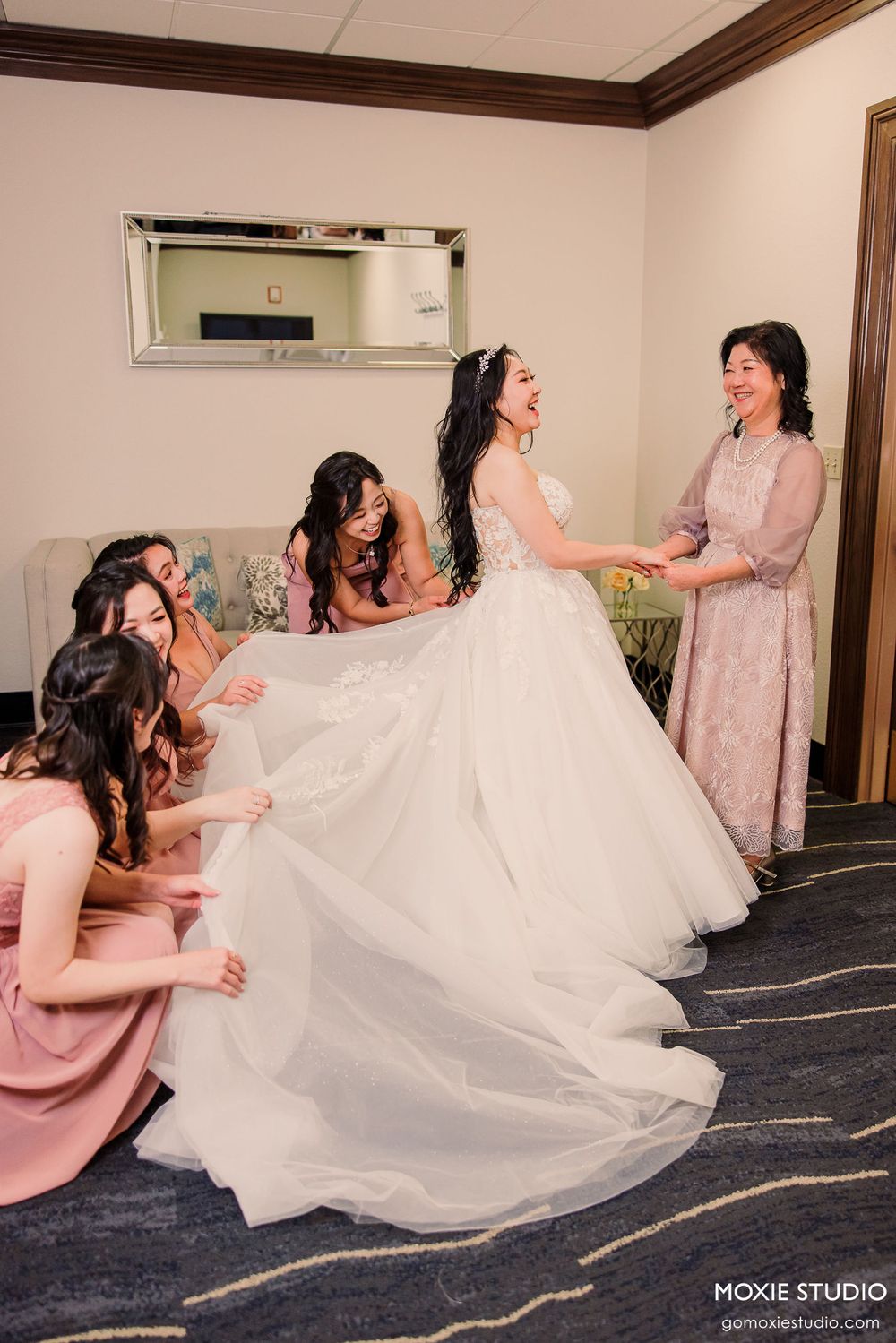 A sequence of four photos showing bridesmaids in pink dresses reacting joyfully to the bride's wedding dress reveal.