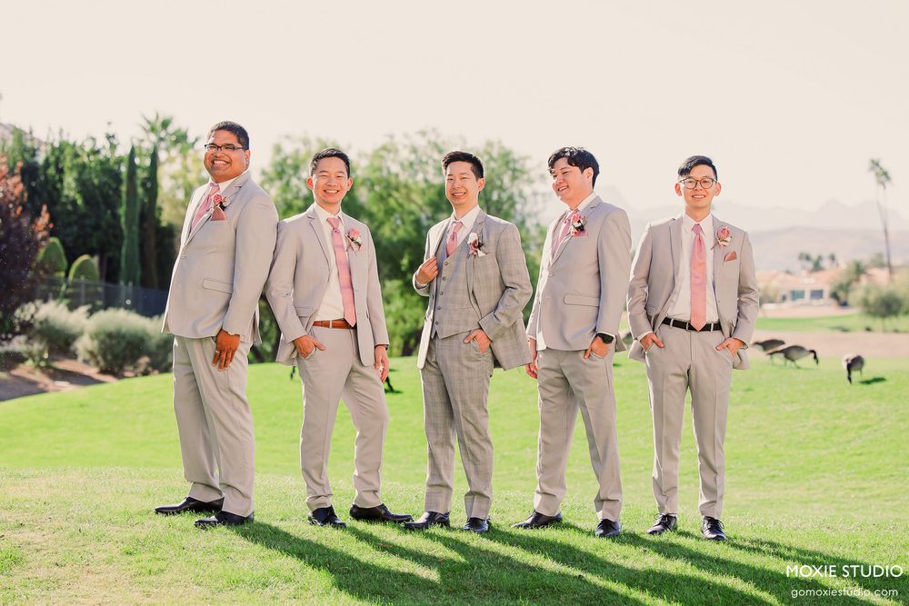 Groomsmen in light gray suits pose together on a grassy lawn during a wedding photoshoot.