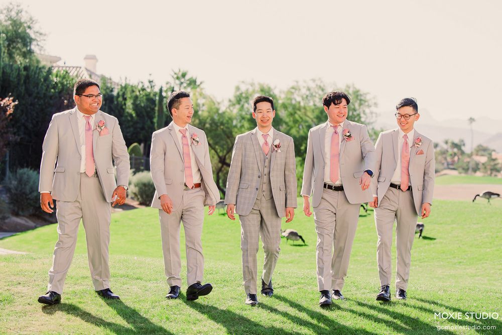 Groomsmen in light beige suits walk in a line on grass with colorful socks adding a playful touch.