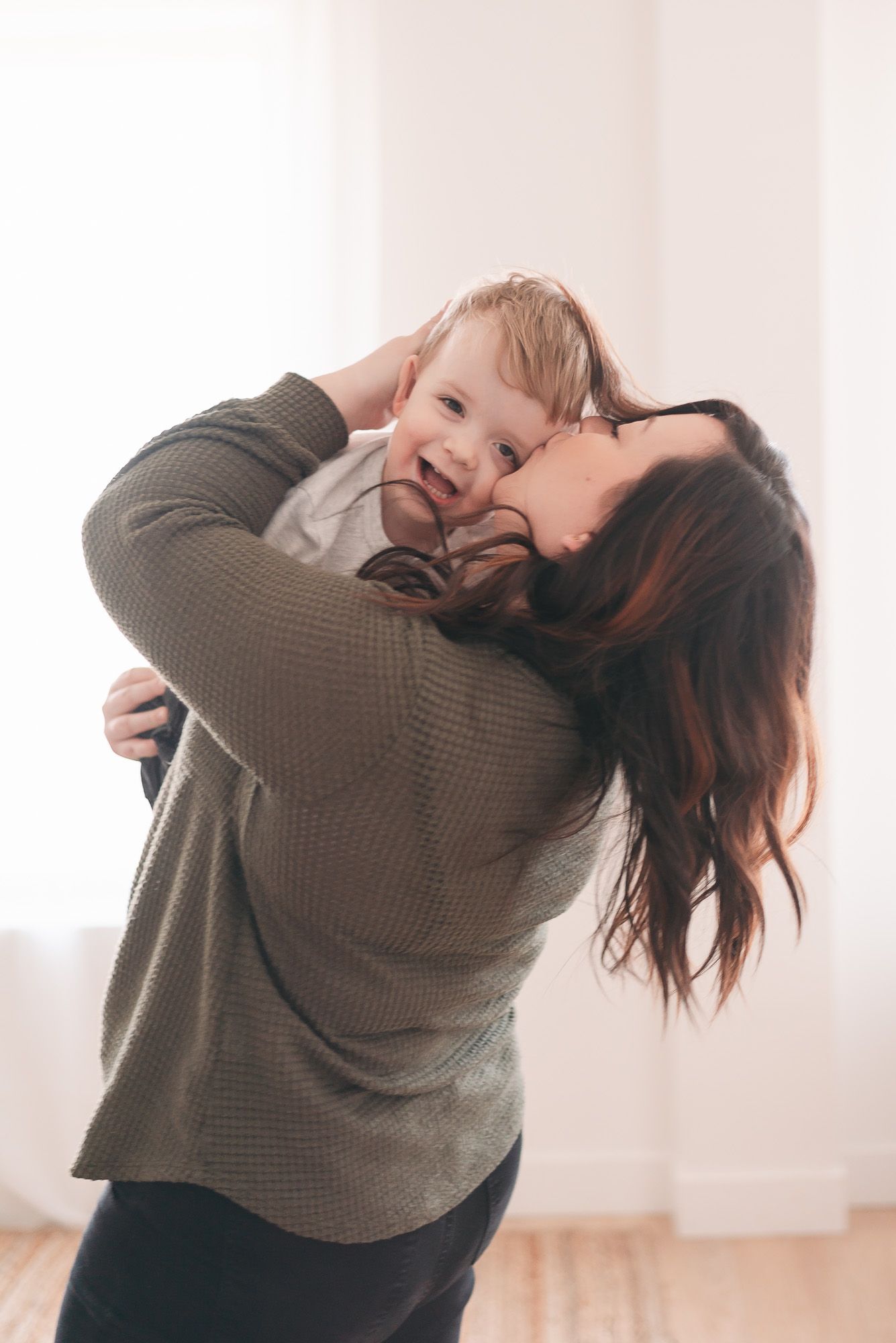 Joyful mother and child playing and laughing together in bright indoor setting.