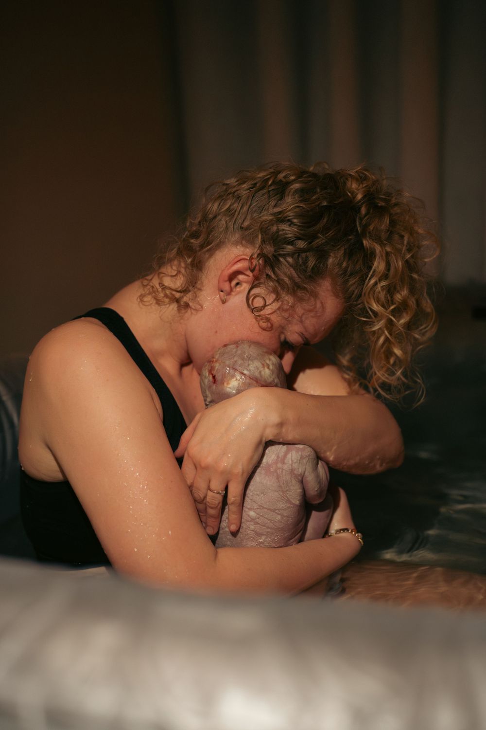 vrouw houdt voor het eerst haar baby vast na de geboorte in een bevalbad