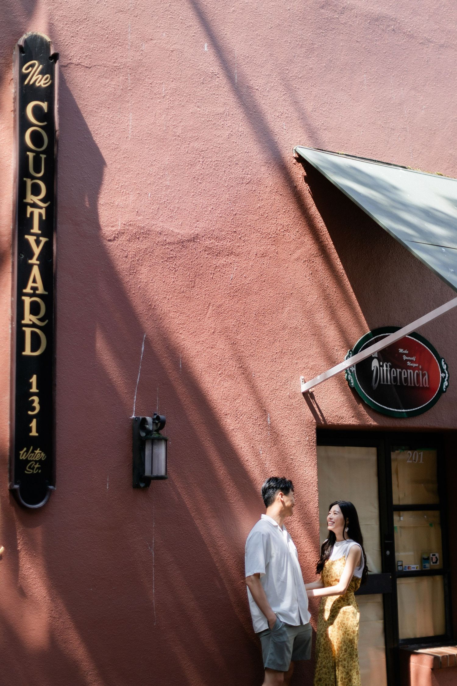 Couple standing together outside The Courtyard 131 building with dramatic sunlight shadows.