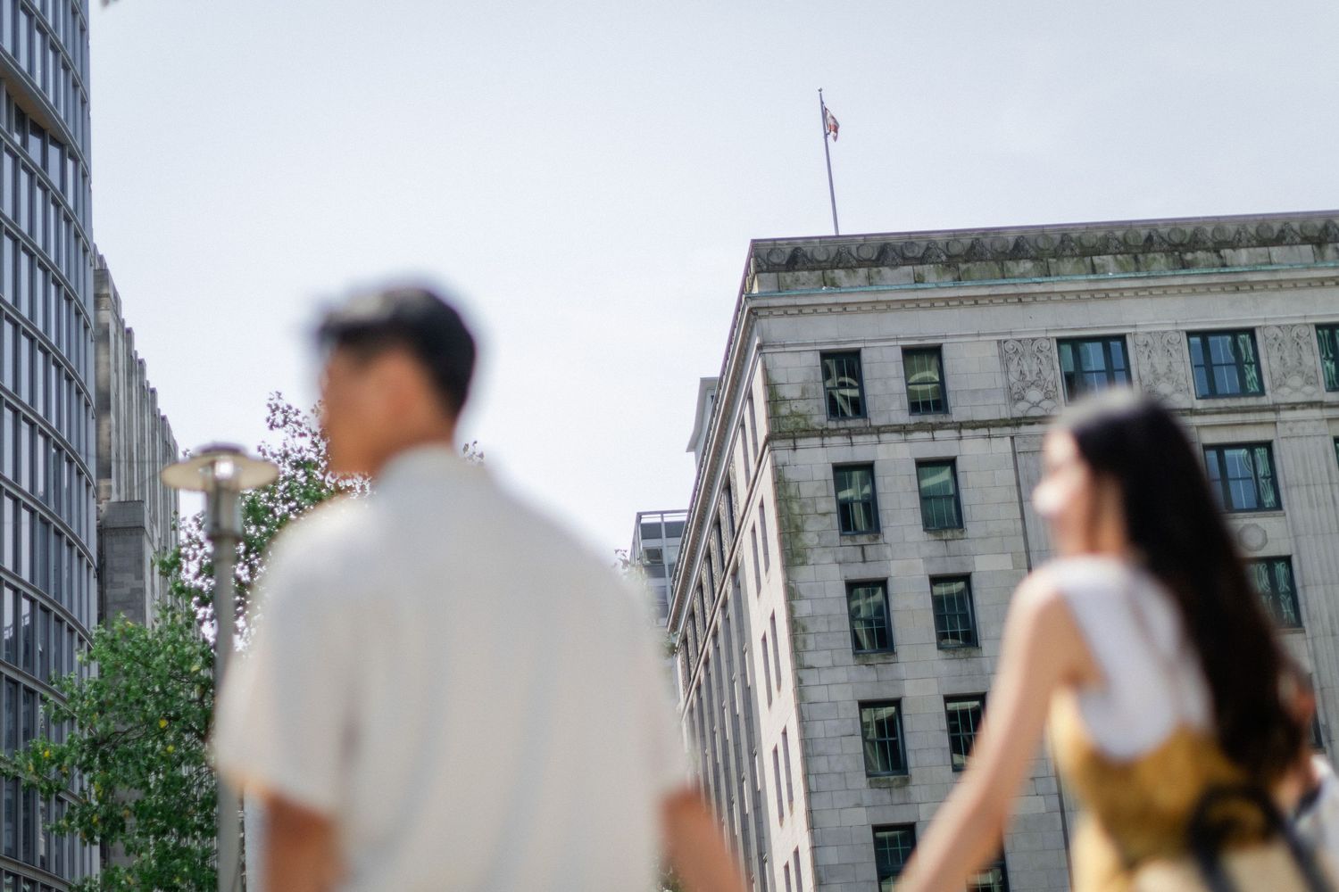Defocused Asian couple holding hands while exploring downtown city streets with tall buildings.
