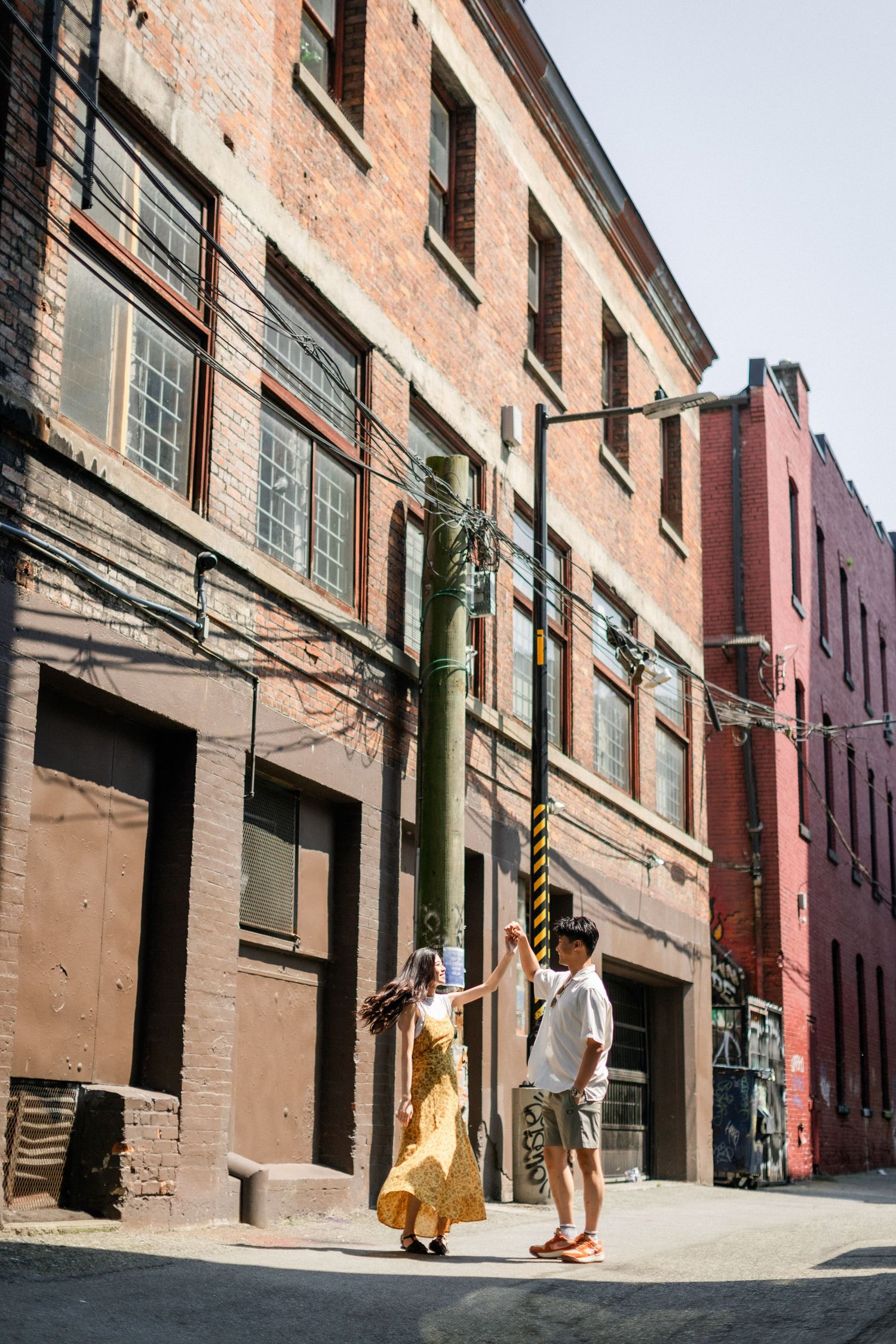 Happy couple dancing together on a sunny urban alley surrounded by rustic brick buildings.