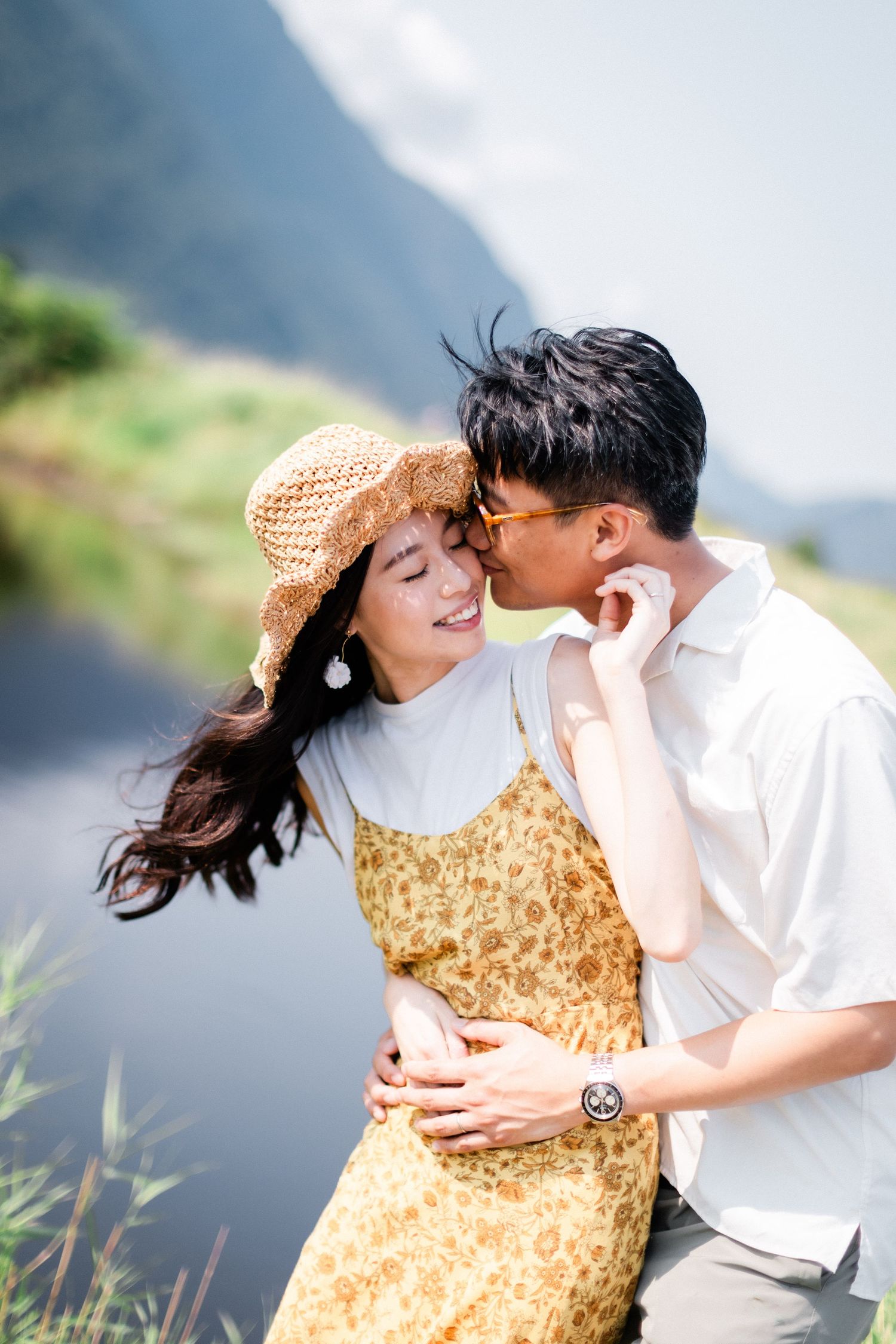 A couple shares a tender moment outdoors, with the man kissing the smiling woman on the cheek.