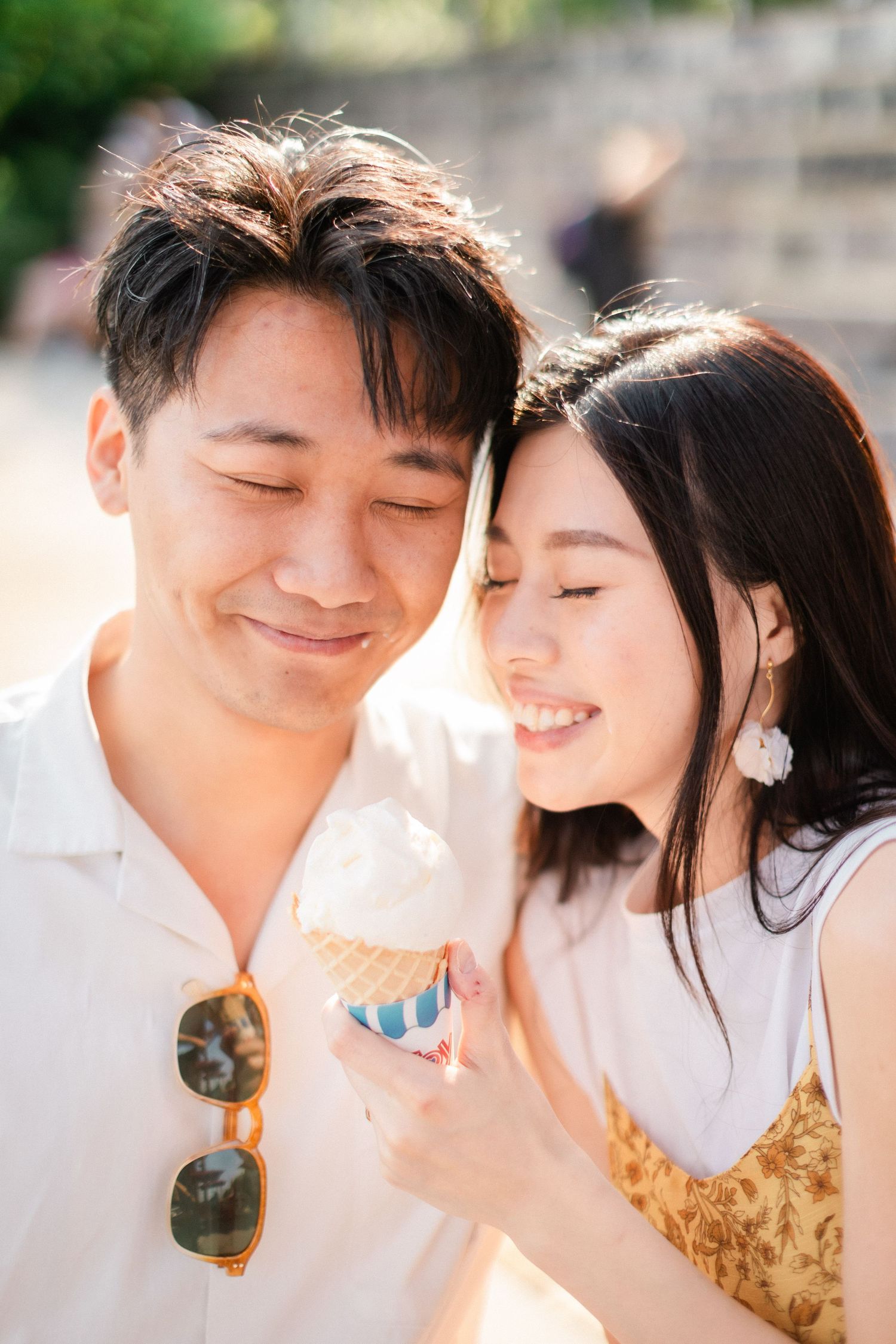 Affectionate Asian couple sharing an ice cream cone together outdoors in warm sunlight.