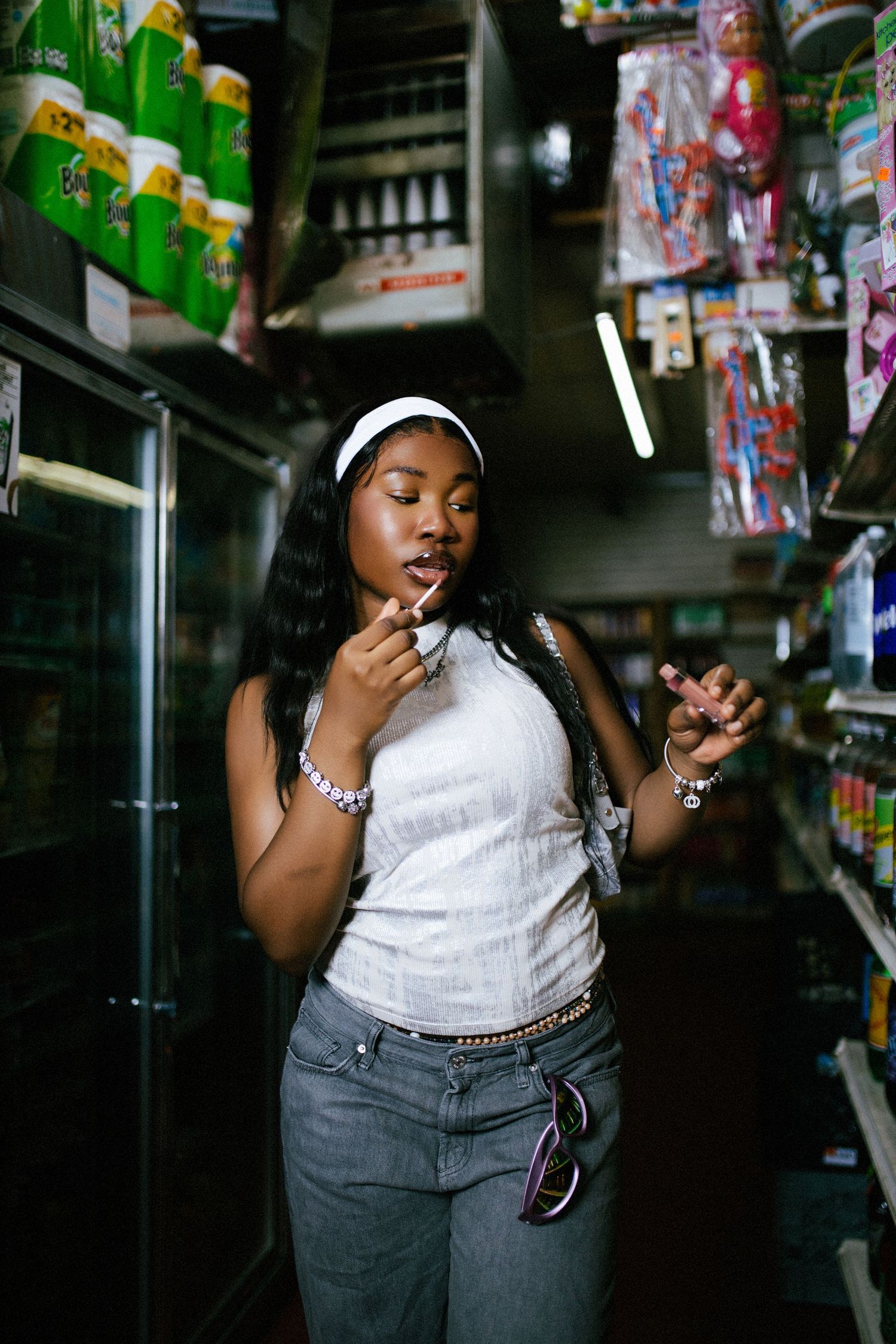 Candid convenience store photo with person in white tank top and jeans among shelves.
