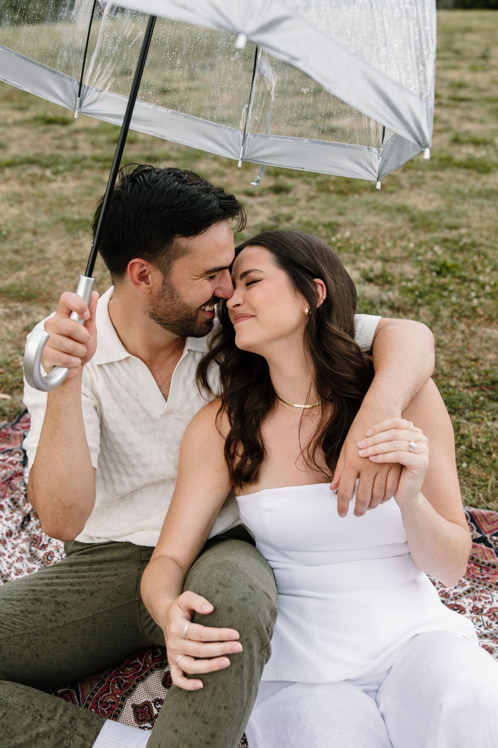 A romantic picnic scene with a white umbrella on a blanket as a couple shares an intimate moment together.