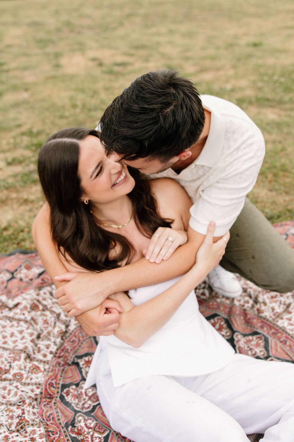 Couple sharing an intimate moment while sitting on a patterned blanket in a grassy field.