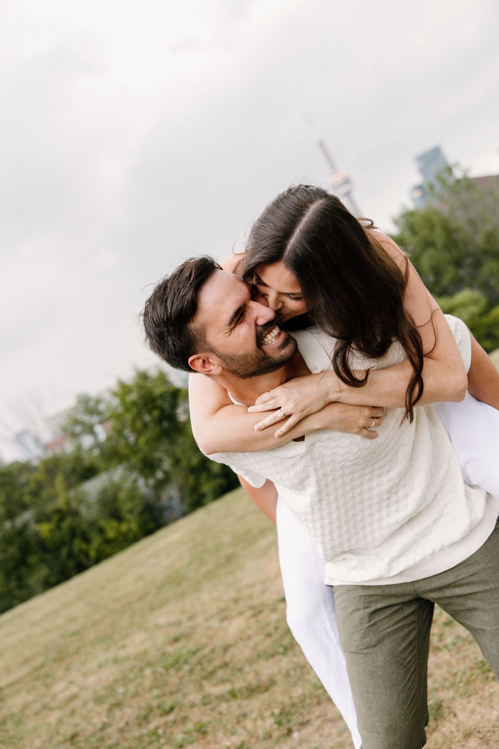 A joyful moment of playful piggyback ride on a grassy hill with the city skyline in the background.