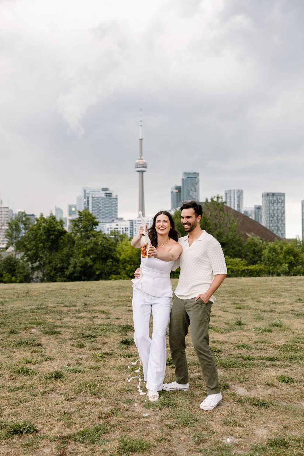 A happy couple shares a moment in front of the Toronto skyline with CN Tower on a cloudy day.