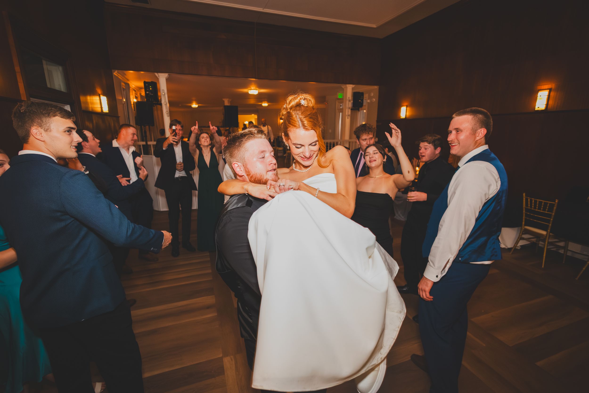 Wedding guests dancing and celebrating on a warmly lit dance floor at an indoor reception.