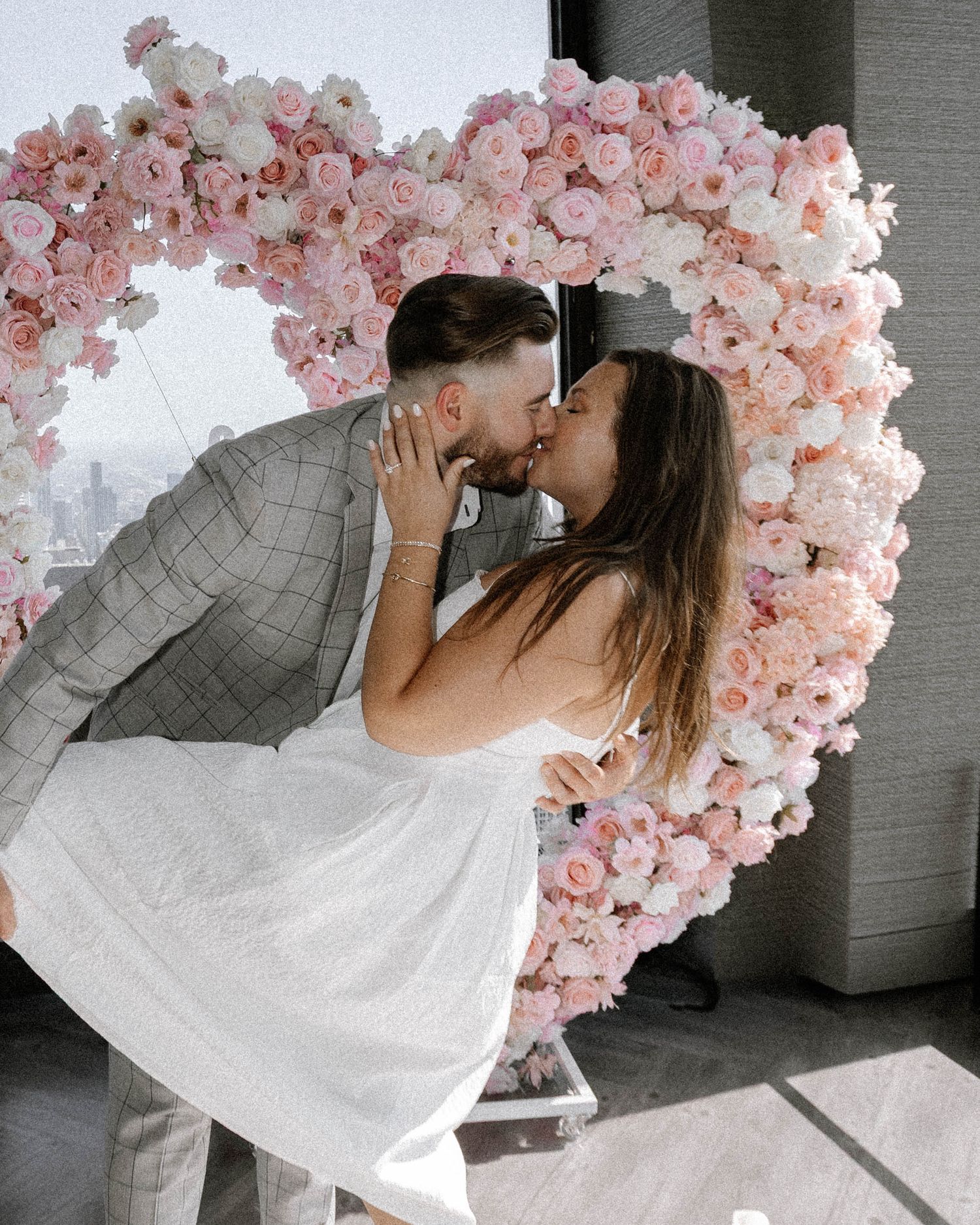 A tender romantic moment between a couple against a pink heart-shaped floral wall display.