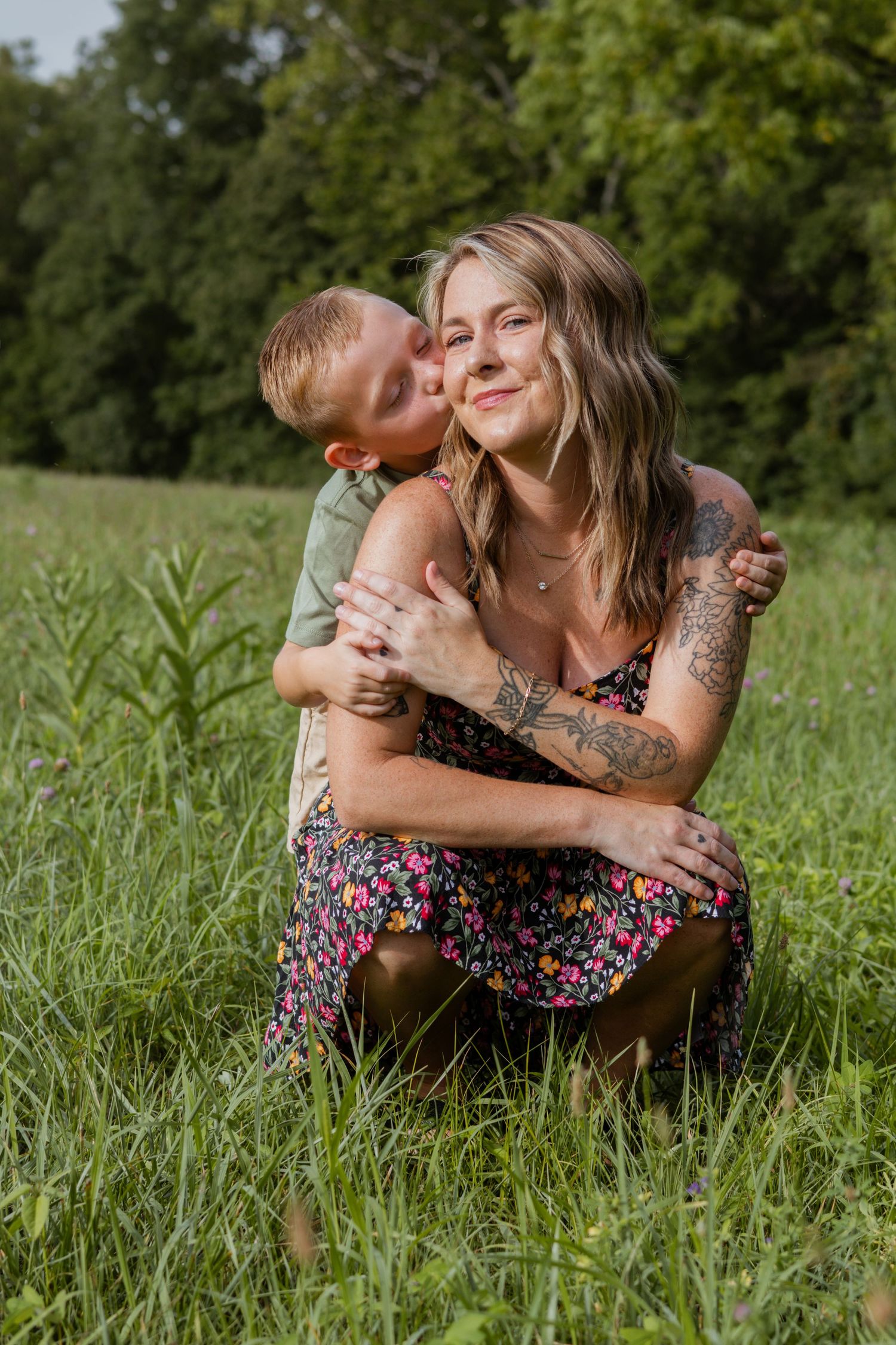 Person cuddles with brown chicken while sitting in sunny meadow with wildflowers.