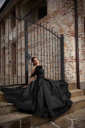 A dramatic black dress flows across stone steps against a brick wall backdrop.