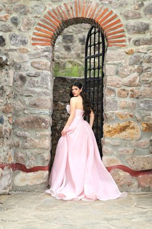 A pink gown creates elegant silhouettes against stone archways and walls.