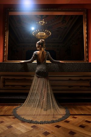 An elegant figure in a flowing sheer gown poses dramatically in an ornate ballroom setting.