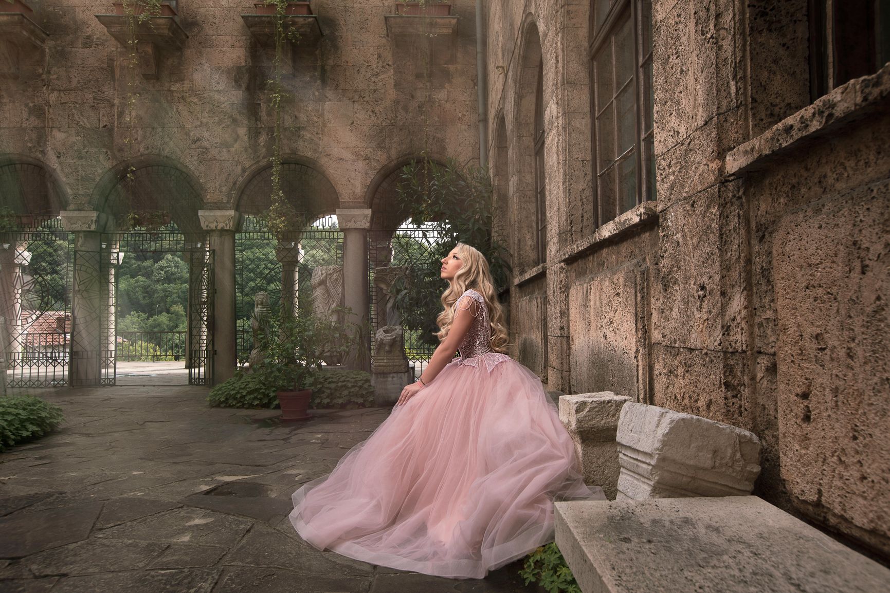 Flowing pink ballgown photographed in dramatic stone archway setting.