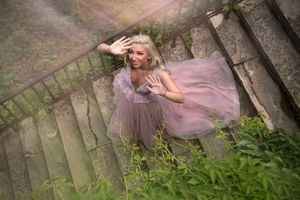 Dreamy portrait in pink tulle dress on stone steps surrounded by greenery.
