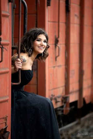 A figure in black leans against a rustic red train car in an artistic portrait series.