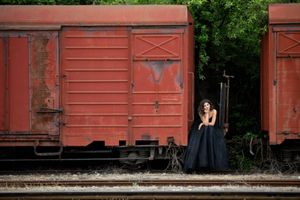 Red train cars line up on railroad tracks with greenery in the background.