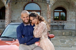 A romantic couple poses together against a brick archway background.