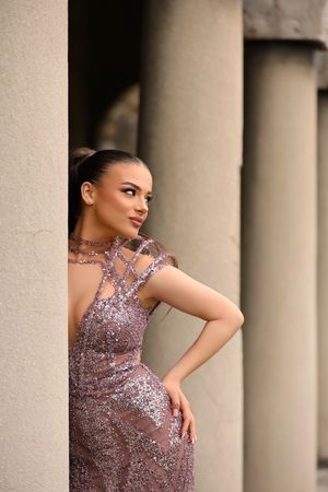 Woman in elegant sequined mauve gown posing gracefully between stone columns.