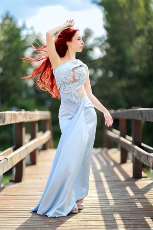 Woman in flowing light blue dress dancing gracefully across a wooden bridge in summer.