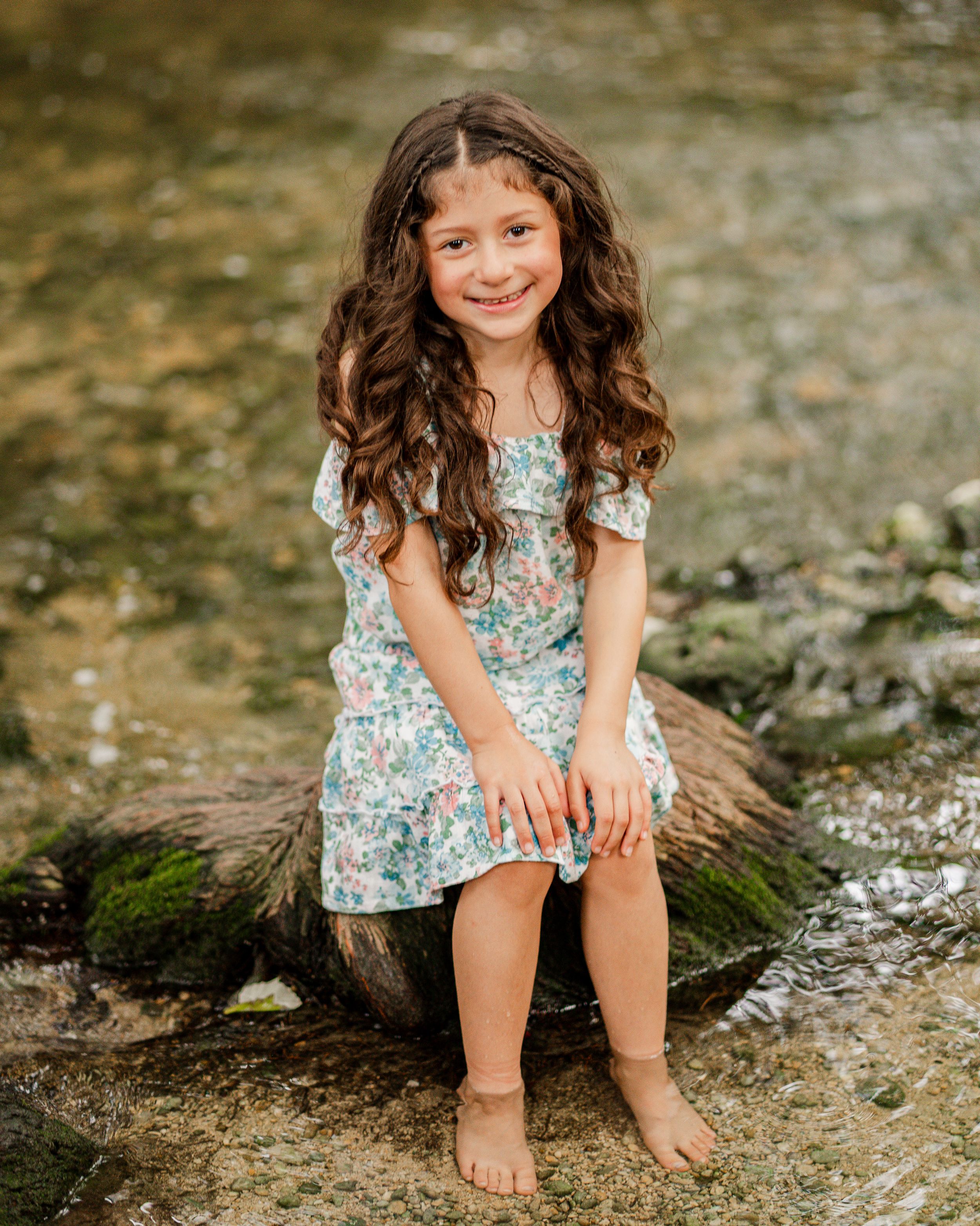 Young girl in floral dress plays by a creek bed in a series of candid outdoor nature photographs.
